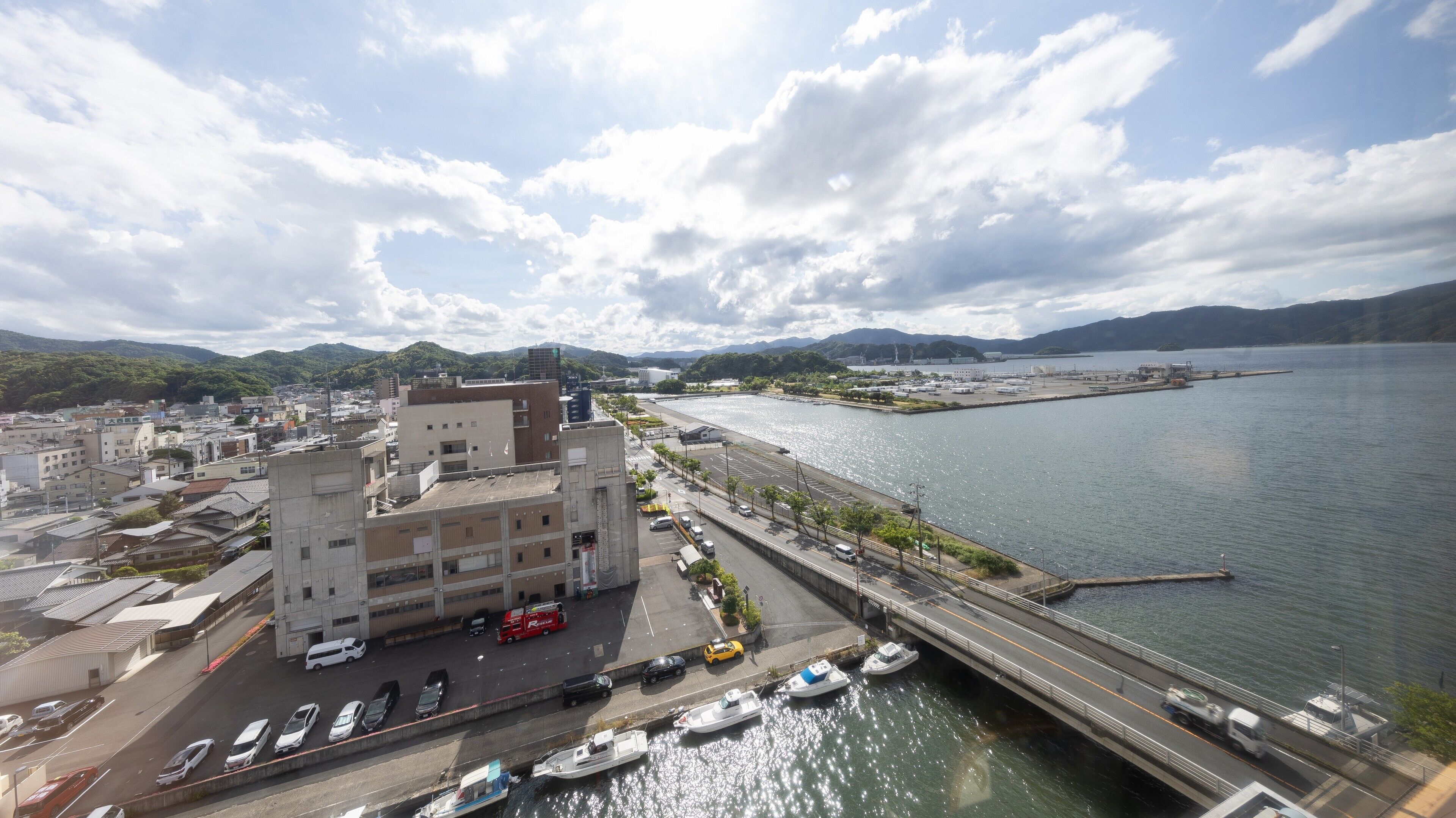A waterfront view with a bridge, boats, and a parking area.