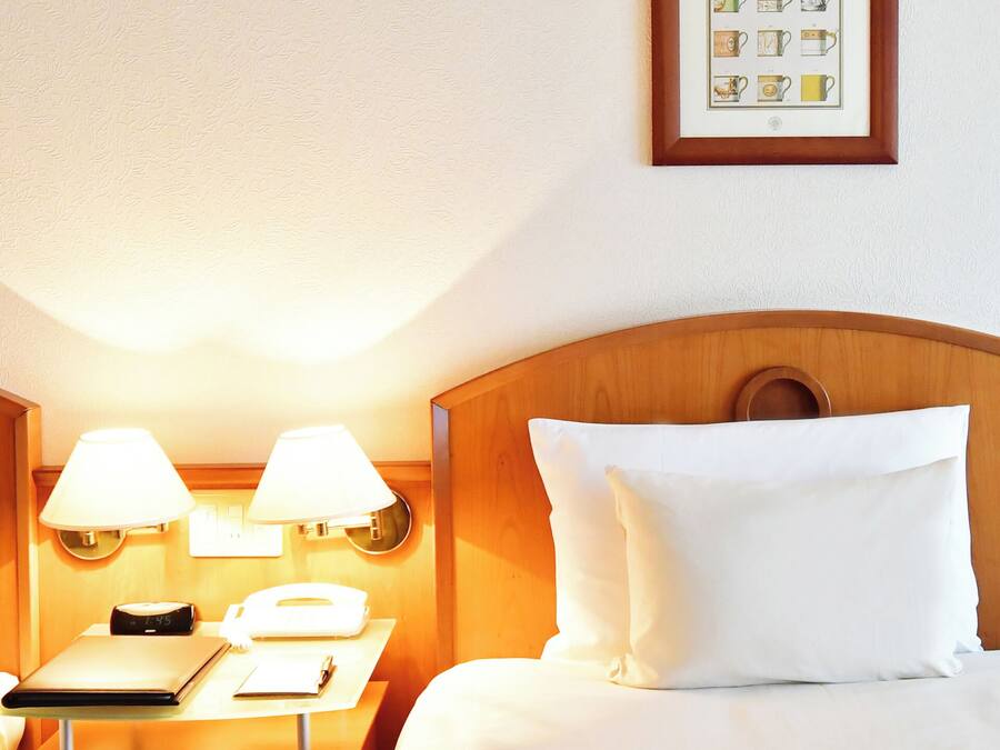 Ett hotellrum med två sängar, var och en med en sänggavel i trä, vita sängkläder och sänglampor. Mellan sängarna står ett litet bord med en telefon och ett anteckningsblock.