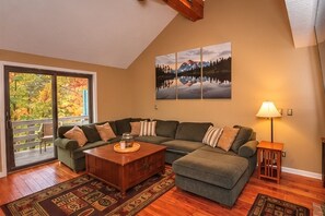 A living room with a sectional sofa, a coffee table, and a lamp. There is a sliding glass door leading to a balcony.