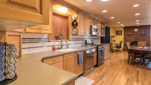 A modern kitchen with wooden cabinets, stainless steel appliances, and a dining area with a brick fireplace. - Family Crash Pad near SLC (Farmington)