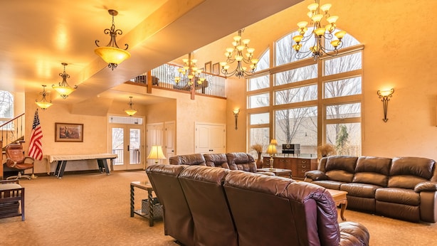 A spacious living area with leather sofas, a high ceiling with chandeliers, large windows, and a flag on the wall. - Family Crash Pad near SLC (Farmington)