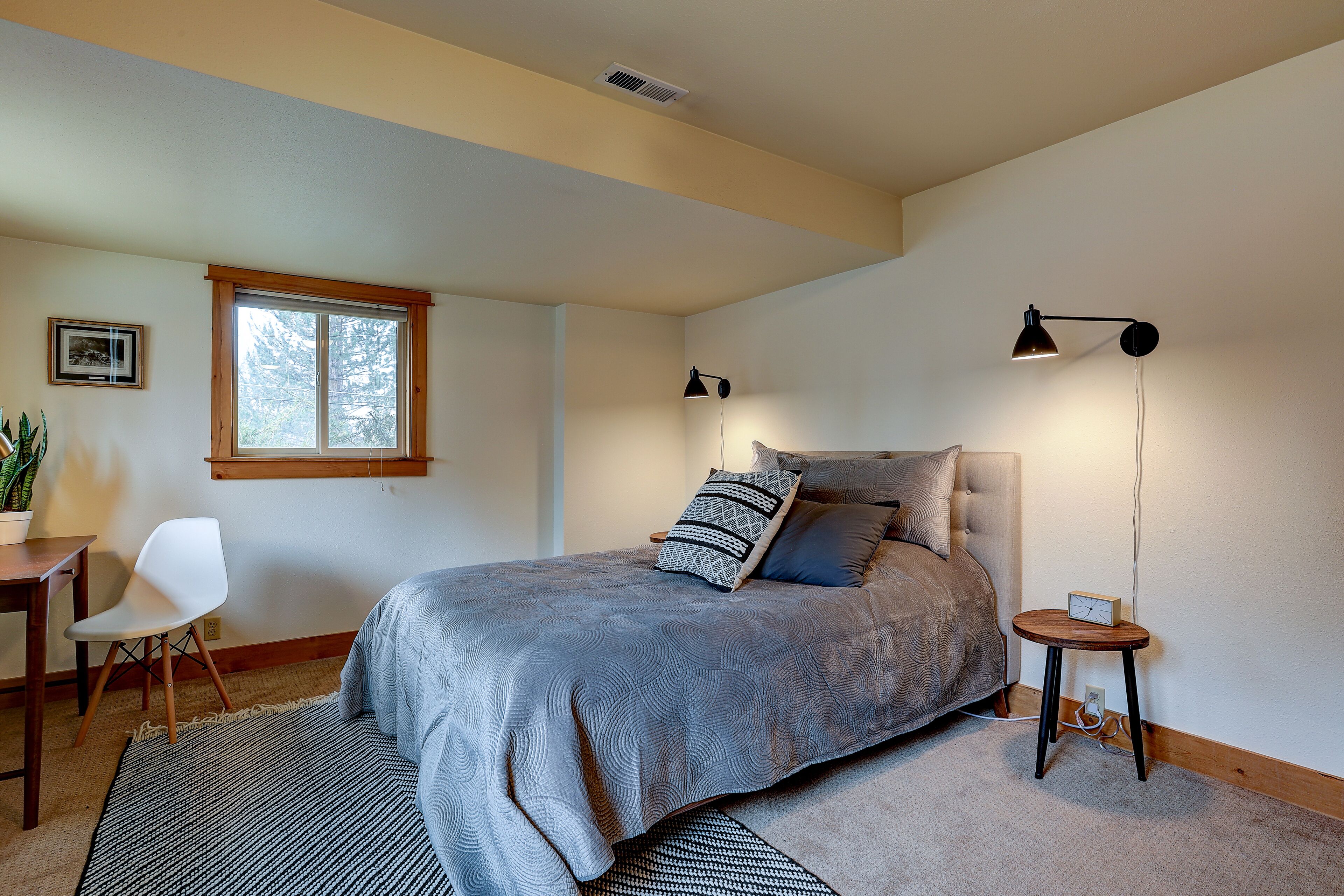 Un dormitorio con cama, mesita de noche, lámpara, silla y ventana.