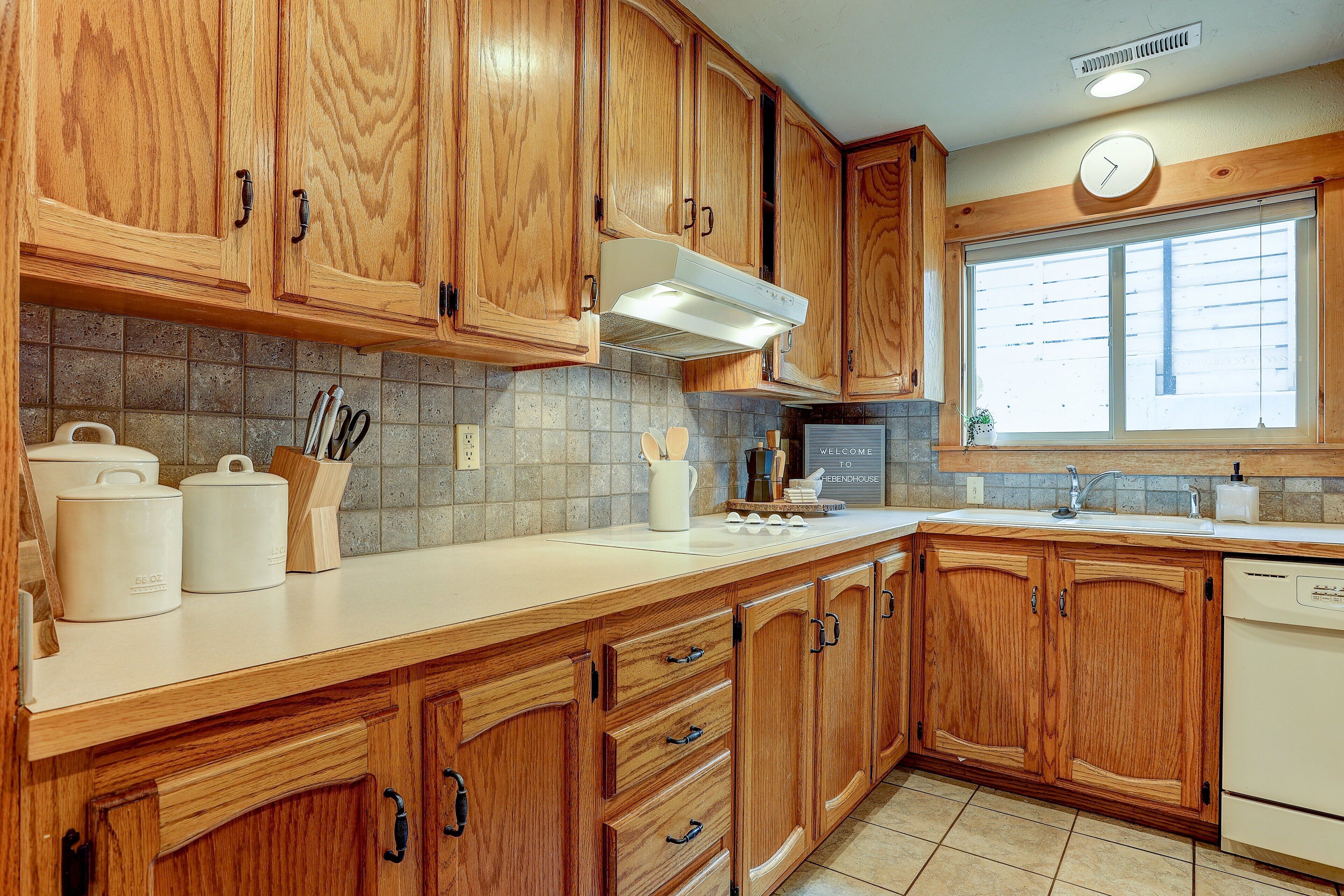 A kitchen with wooden cabinets, a white countertop, and a window with blinds.