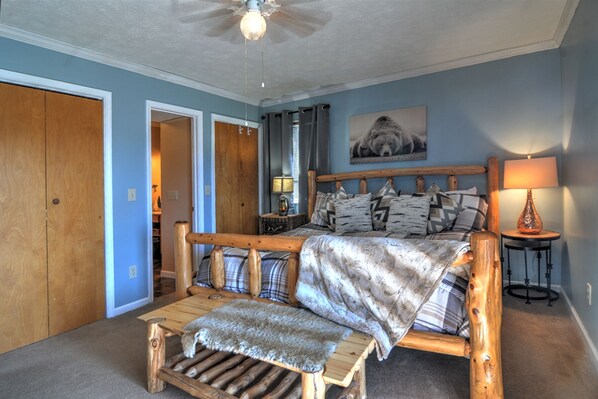 A bedroom with a wooden bed, a bench, a lamp, and a ceiling fan.