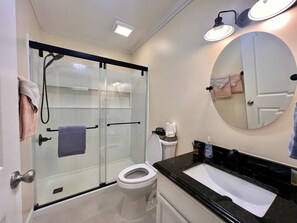 A modern bathroom with a glass-enclosed shower, a toilet, a sink with a black countertop, and a mirror with a round frame.