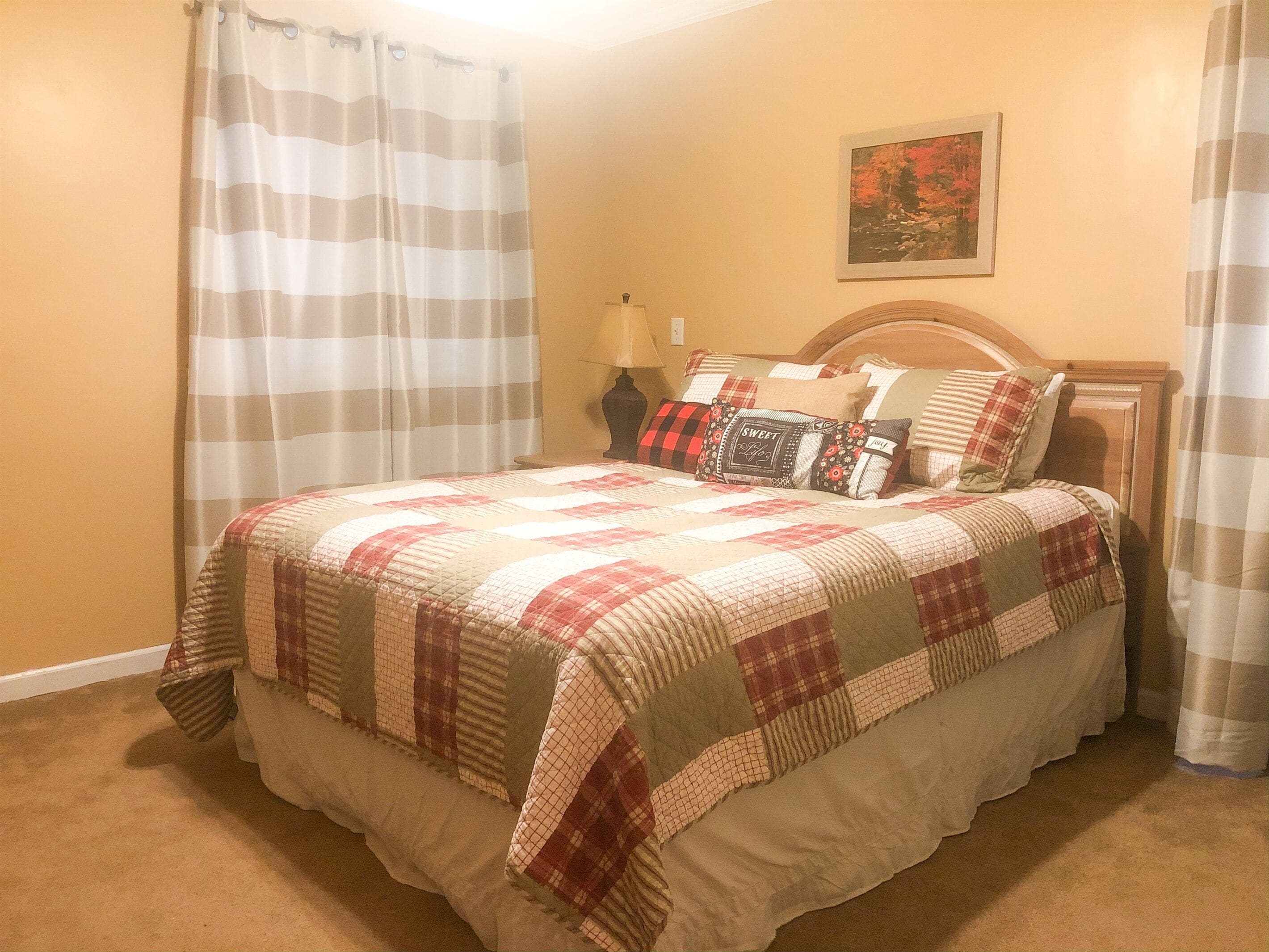 Una cama bien hecha con colcha, cabecera de madera y mesita de noche con lámpara.
