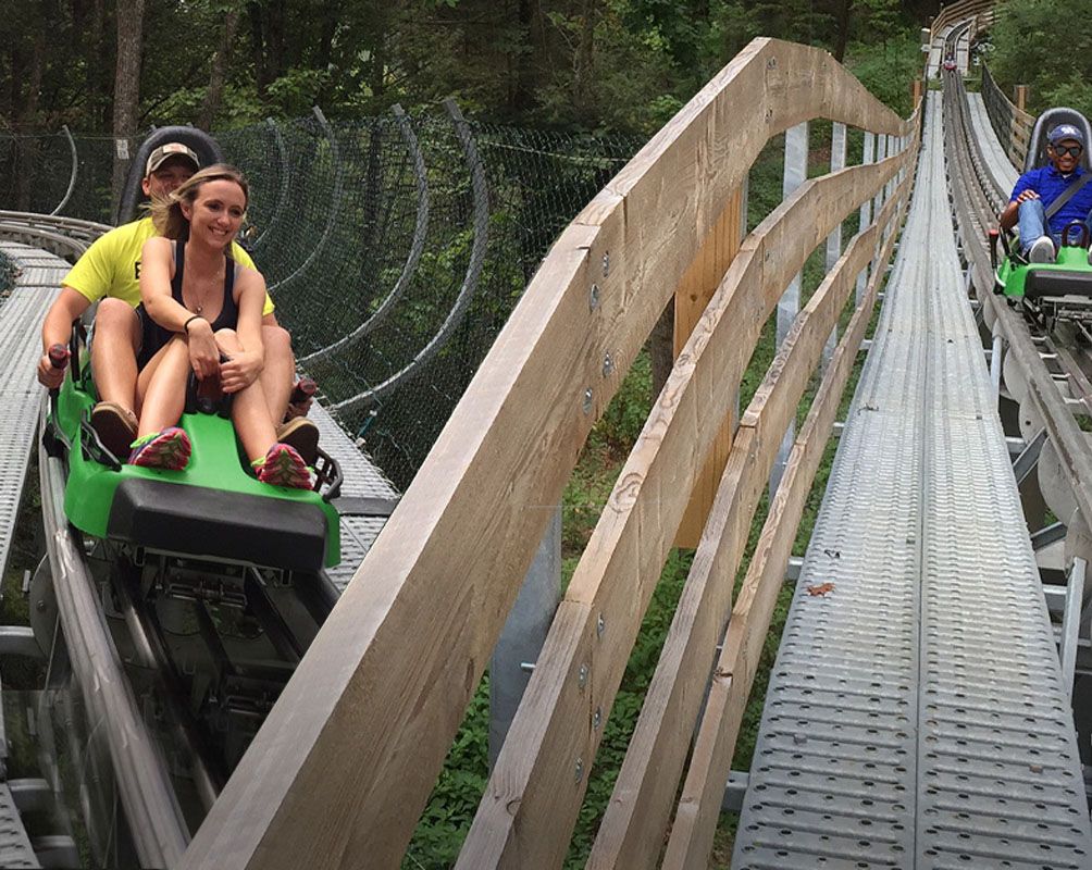 A wooden roller coaster track with two green cars and a person in a yellow shirt.