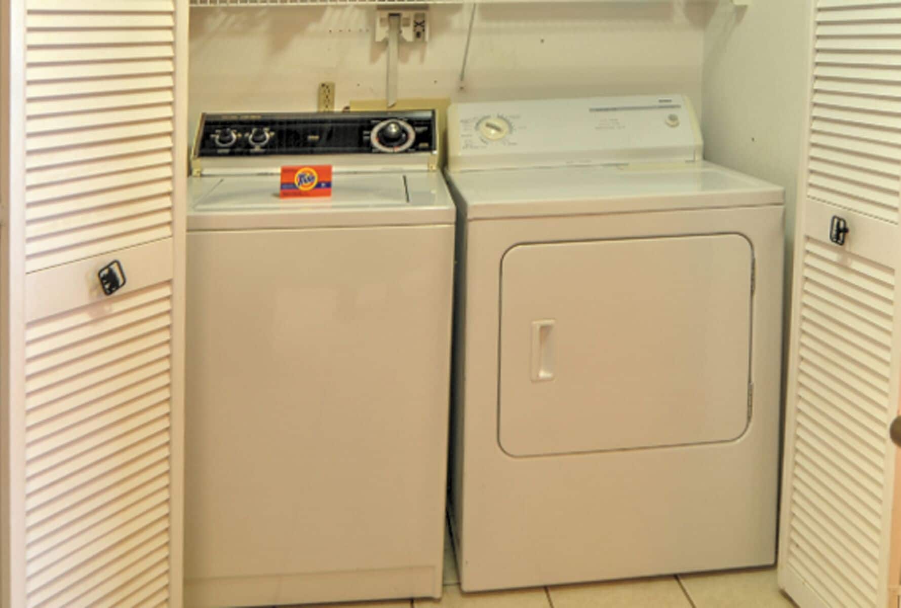 A compact laundry room with a front-loading washer and dryer, a control panel, and a door with a handle.