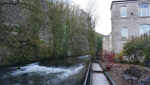 Un río fluye por una zona boscosa con un edificio de piedra a la derecha.