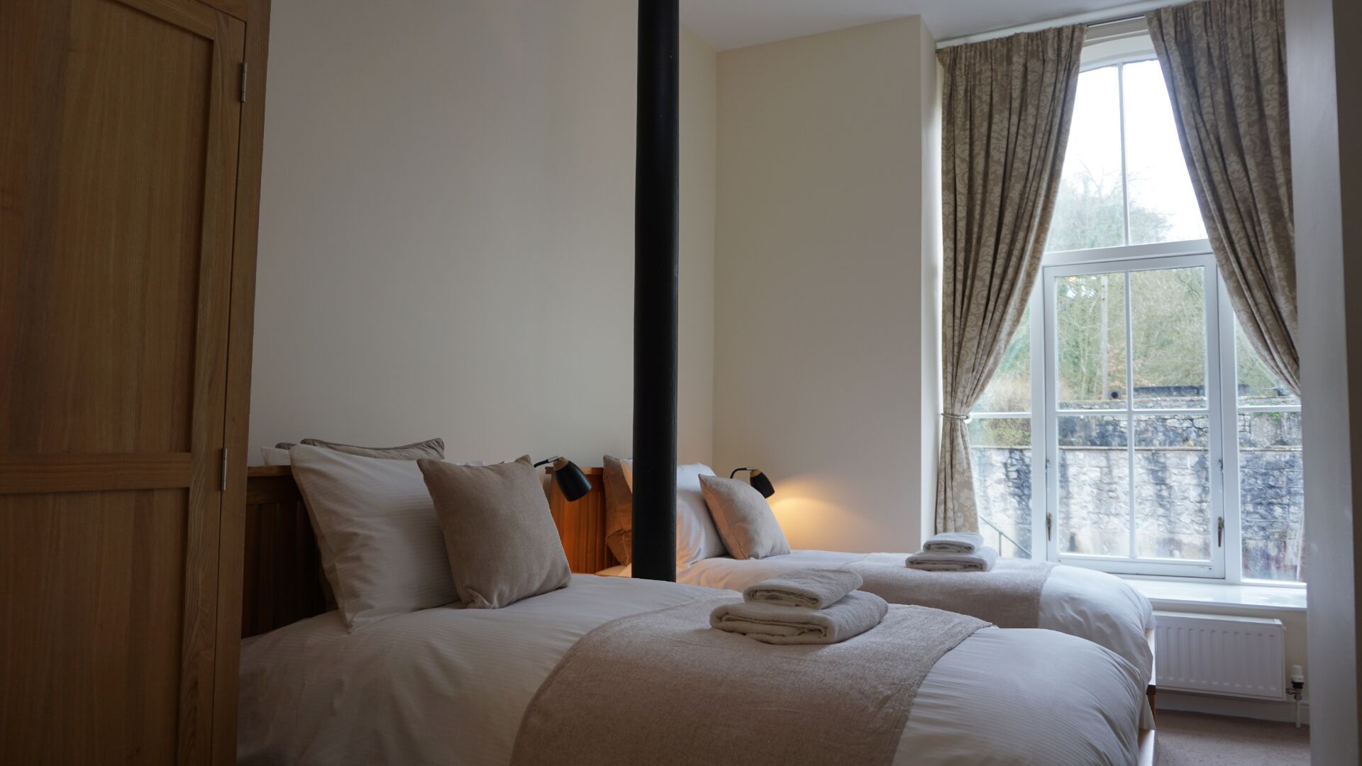 Una camera da letto con due letti, un armadio, una finestra con tende e un termosifone.