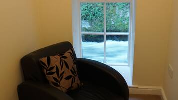 A corner of a room with a black leather chair and a window with a view of a river.