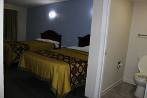 A hotel room with two beds, a bathroom with a toilet, and a visible light switch on the wall.