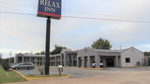 A Relax Inn hotel with a large sign, a parking lot, and a building with multiple floors and a flat roof. - Relax Inn (Canton)