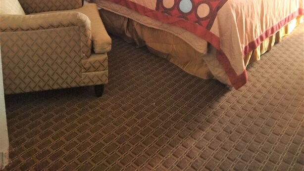 A hotel room with a large bed, a wooden headboard, a patterned armchair, and a window with curtains. - Relax Inn (Canton)
