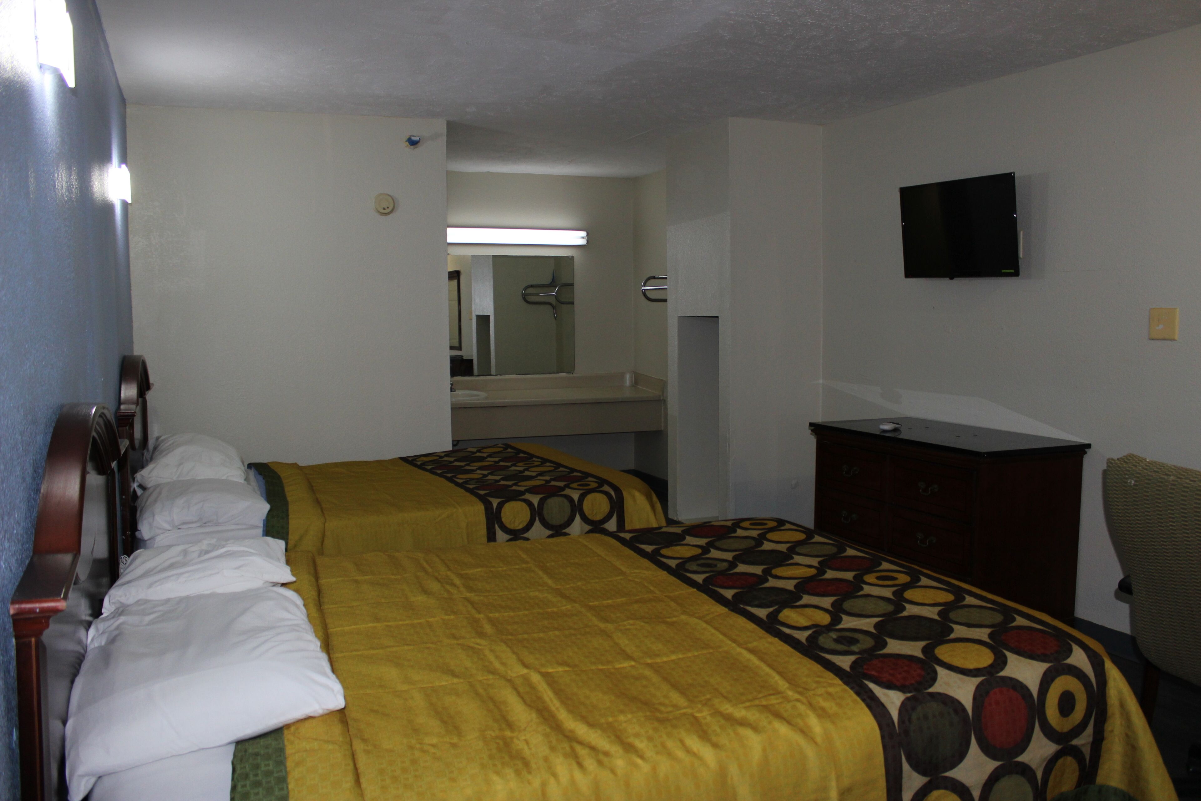 A hotel room with two beds, a television, a dresser, and a mirror.