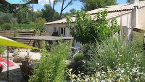 Ein Poolbereich mit Liegestühlen, eine Terrasse mit Tisch und Stühlen sowie ein Haus mit Ziegeldach und Garten.