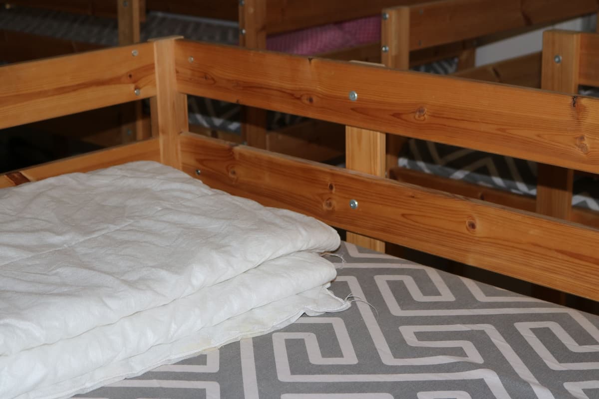 A wooden bunk bed with a white mattress and a patterned pillowcase.