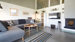 A modern living room with a grey sectional sofa, a round coffee table, a striped rug, a fireplace, a TV, and a bookshelf. - Lovely home in Aabenraa with kitchen (Aabenraa)