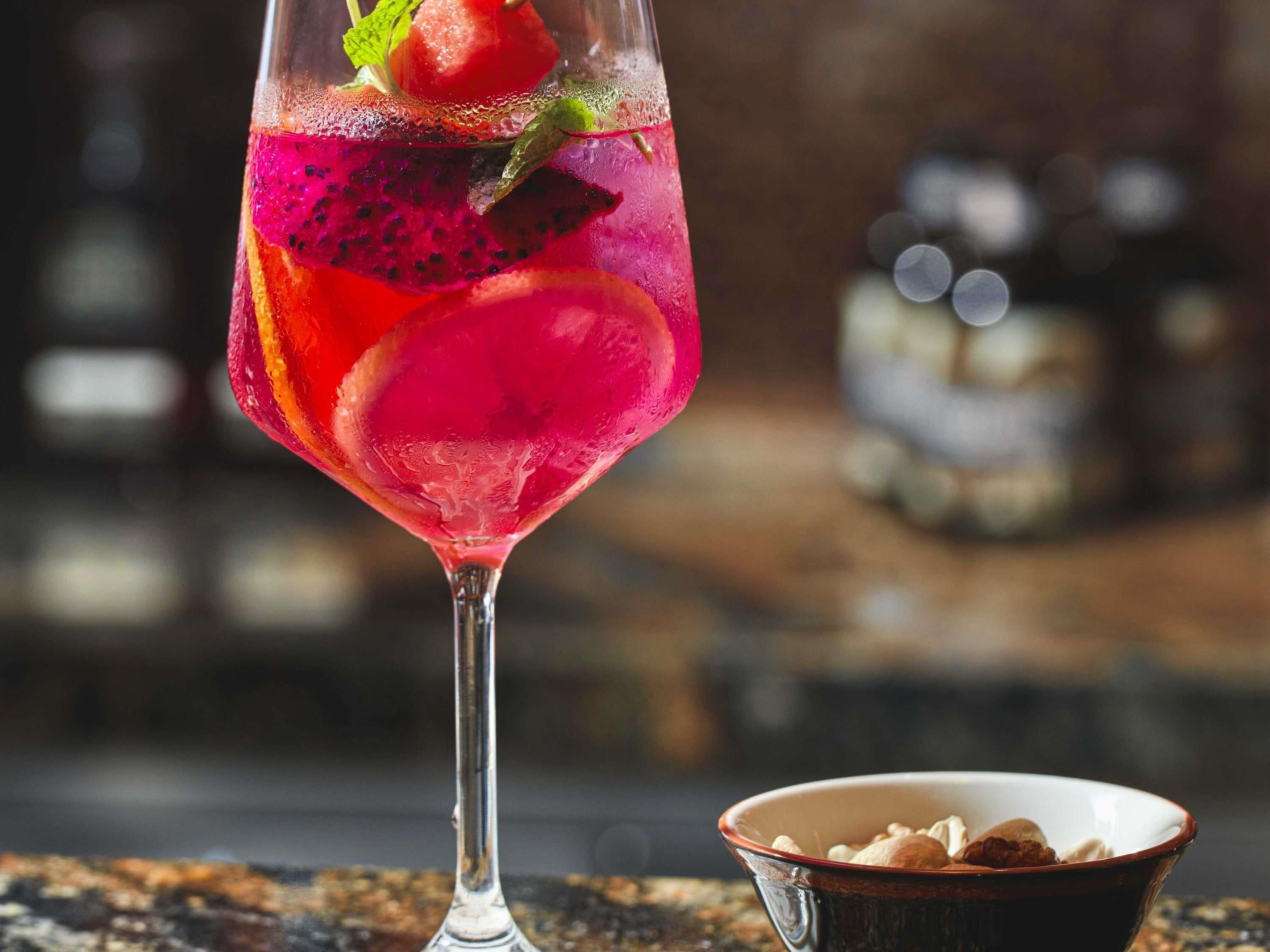 A cocktail glass with a vibrant drink, a mint leaf, and a strawberry garnish.