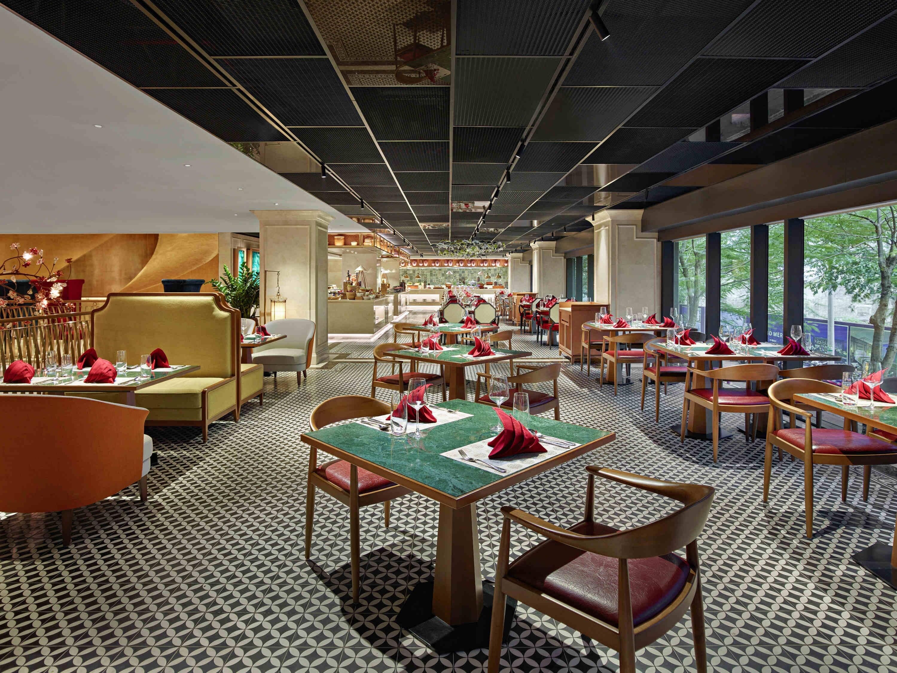 Un restaurante con piso estampado, mesas con servilletas rojas y vista a zonas verdes.