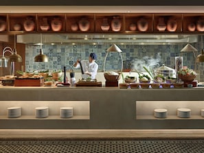 A kitchen with a chef preparing food, a variety of cooking utensils, and a display of copper pots. - Grand Mercure Hanoi (Hanoi)