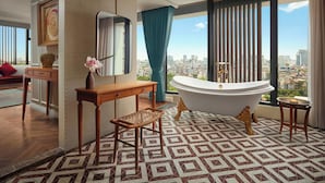 A modern bathroom with a freestanding bathtub, a vanity with a mirror, and a view of the city through large windows. - Grand Mercure Hanoi (Hanoi)