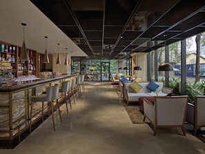 A bar area with a marble countertop, bar stools, and a seating area with sofas and chairs.
