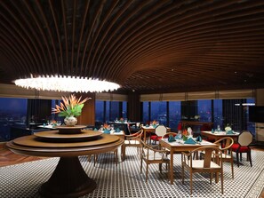 Un restaurant au dĂ©cor moderne, avec une table ronde agrĂ©mentĂ©e dâun vase de fleurs, des chaises en bois et un sol Ă motifs.