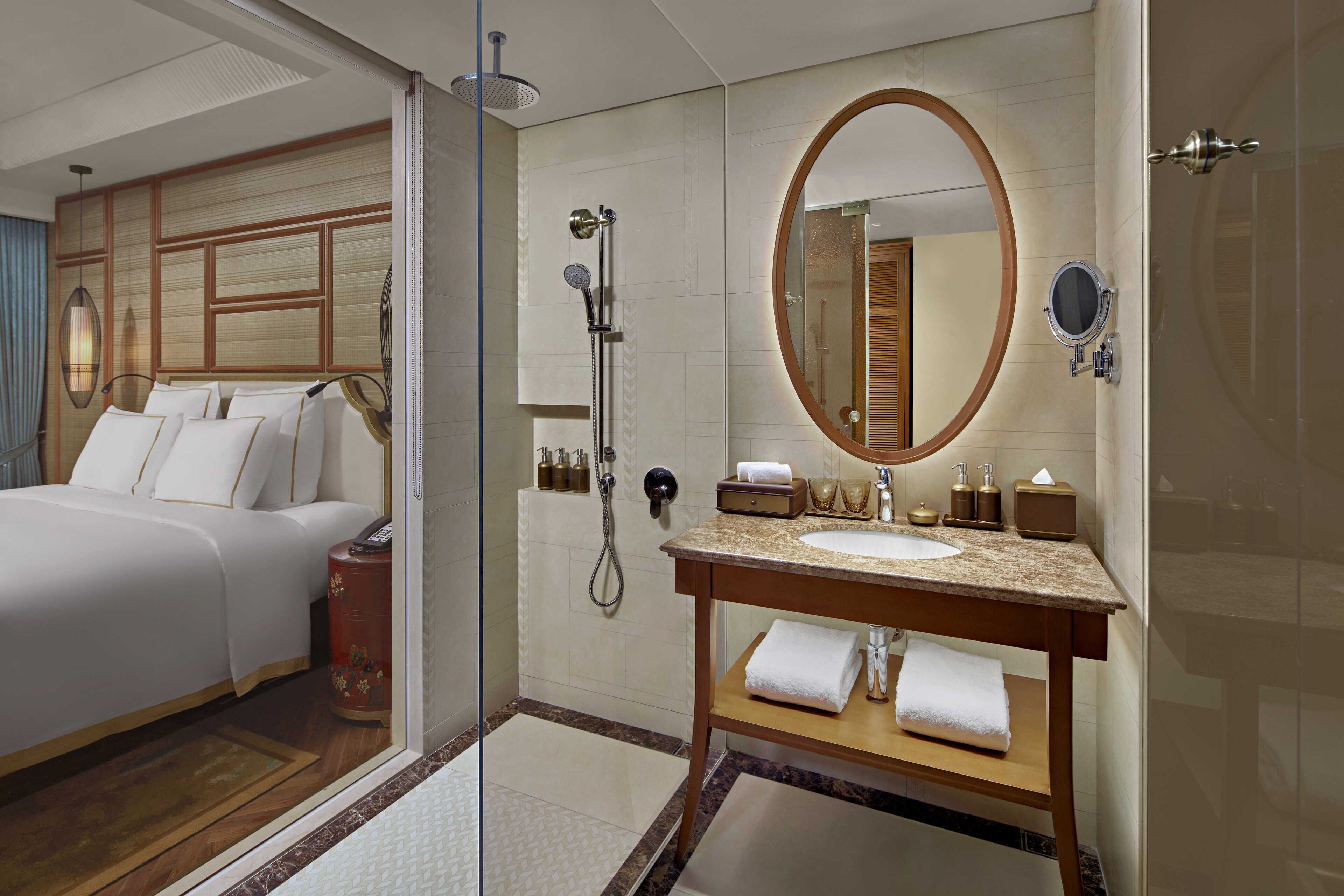 Camera d'albergo con un letto, doccia a vetro, mobile bagno in legno con lavandino e un grande specchio.