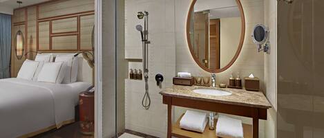 Camera d'albergo con un letto, doccia a vetro, mobile bagno in legno con lavandino e un grande specchio.