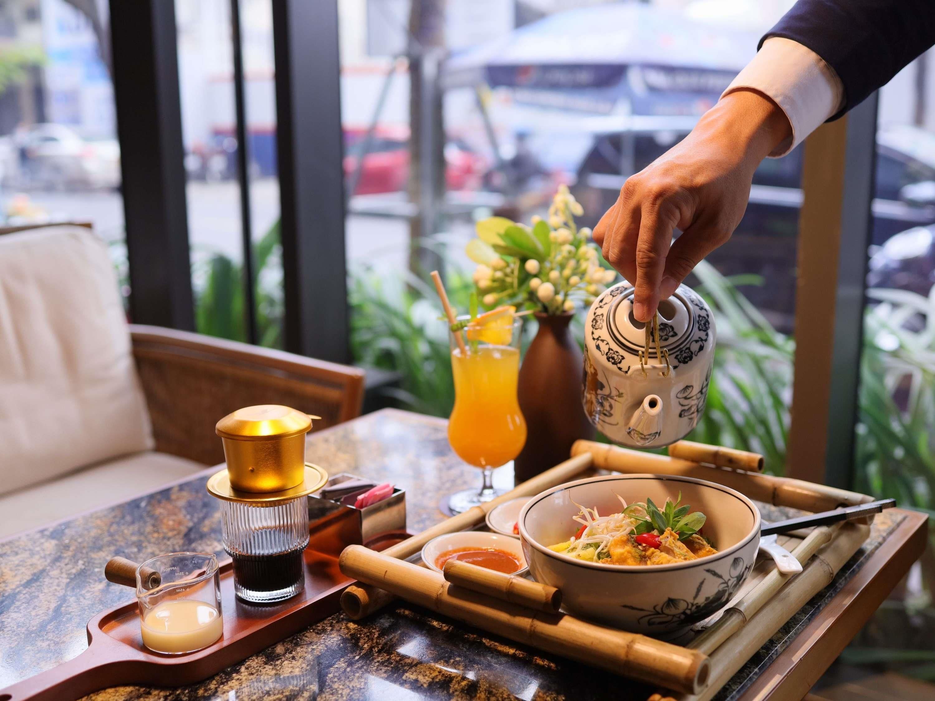 A dining table with a teapot, a glass of orange juice, a bowl of food, and a small cup of tea.
