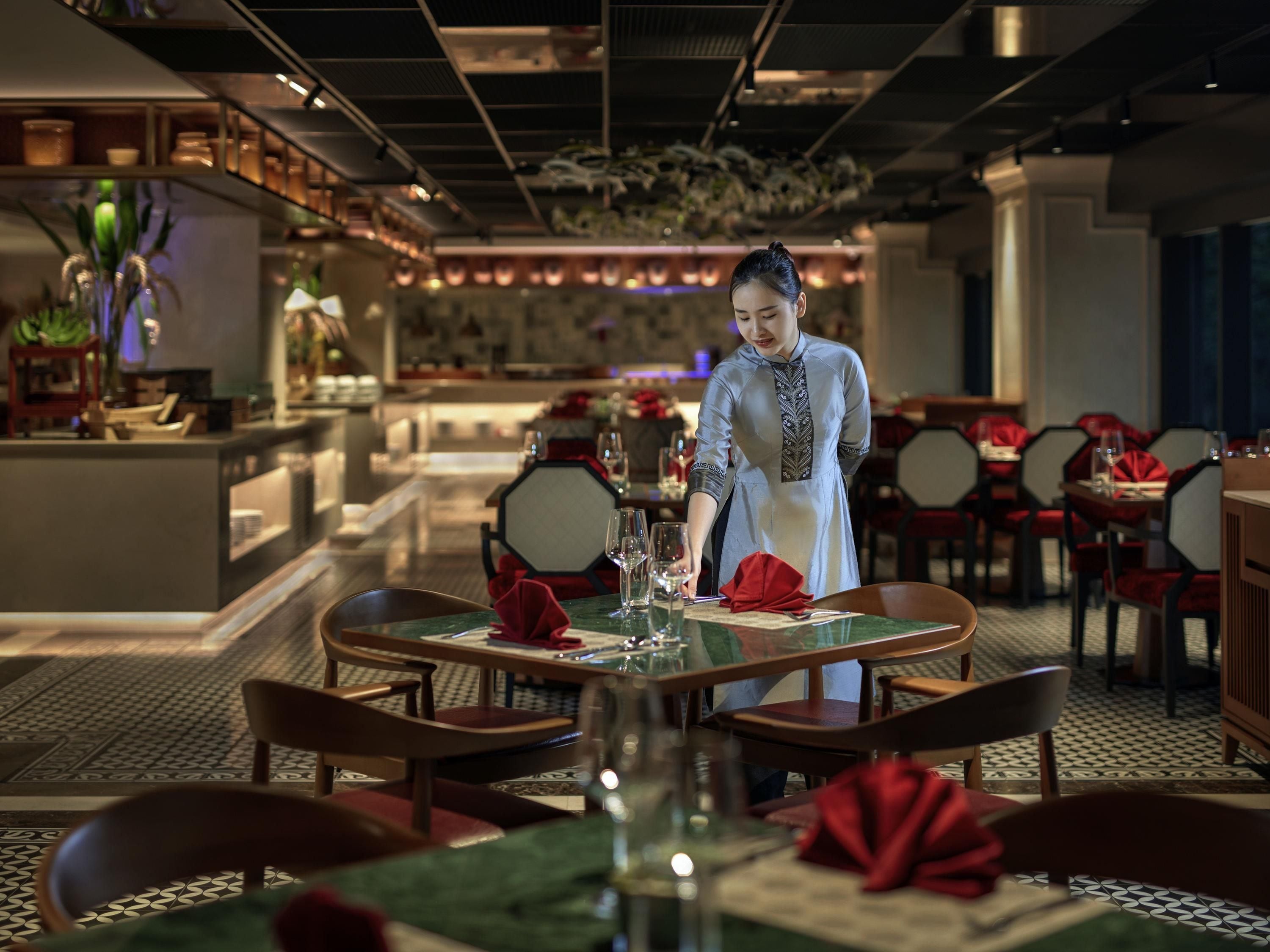 Ein Restaurantinnenraum mit runden Tischen, roten Servietten und einer Bar.