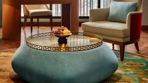 A modern hotel room with a large window, a round coffee table with fruits, a chair, and two lamps. - Grand Mercure Hanoi (Hanoi)