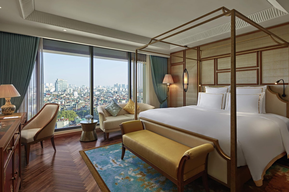 A spacious hotel room with a large bed, a seating area, and a view of the cityscape.