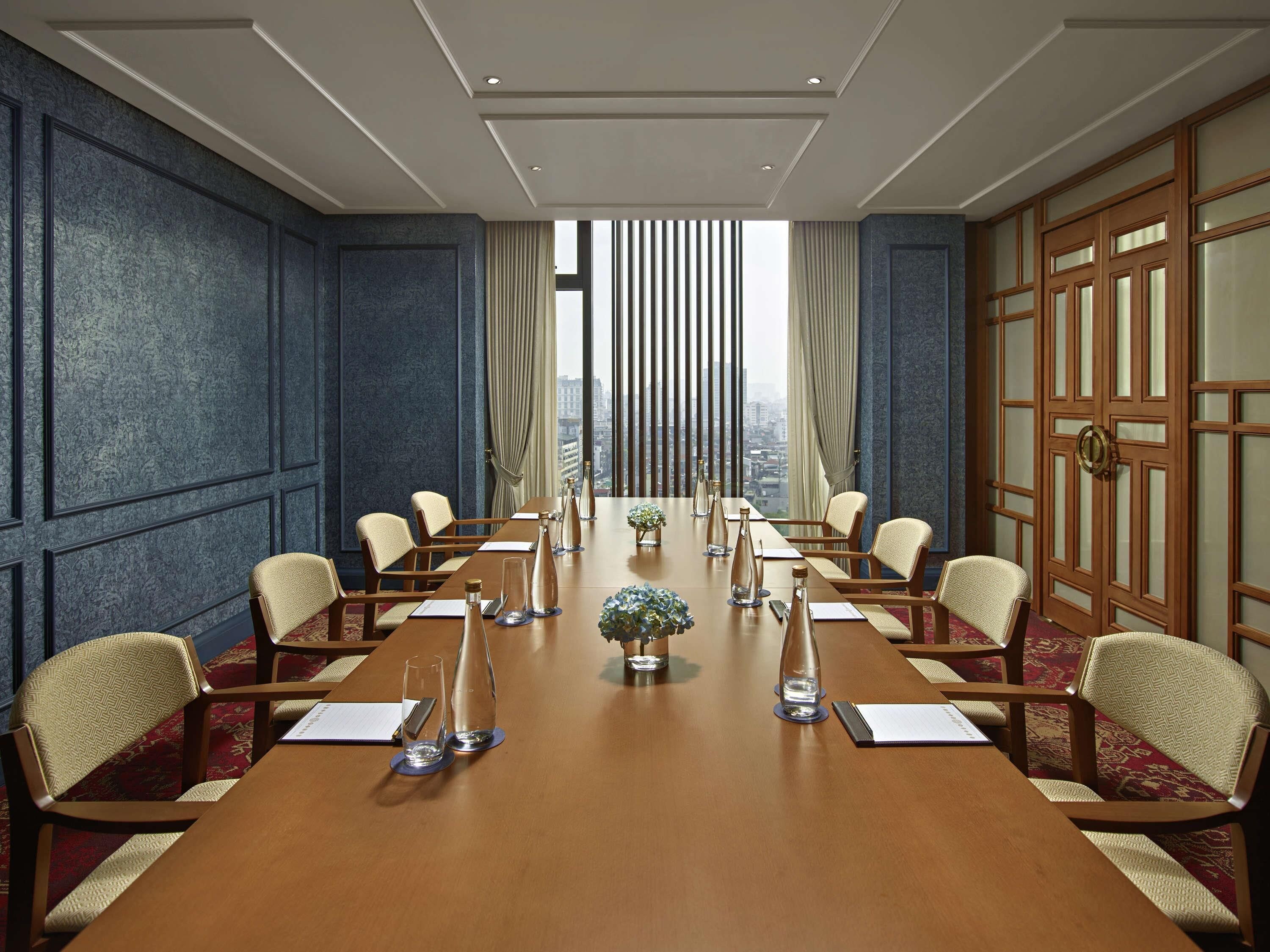 A conference room with a long table, chairs, and a view through large windows.