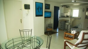A dining area with a glass table and metal chairs, a kitchen with white cabinets, and a living area with a sofa and a coffee table. - Appartement en Bord de Mer,beau Balcon, Plages,sentiers et Commerces à Proximité (Arzon)