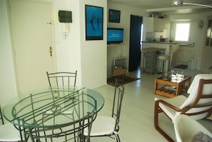 A dining area with a glass table and metal chairs, a kitchen with white cabinets, and a living area with a sofa and a coffee table. - Appartement en Bord de Mer,beau Balcon, Plages,sentiers et Commerces à Proximité (Arzon)