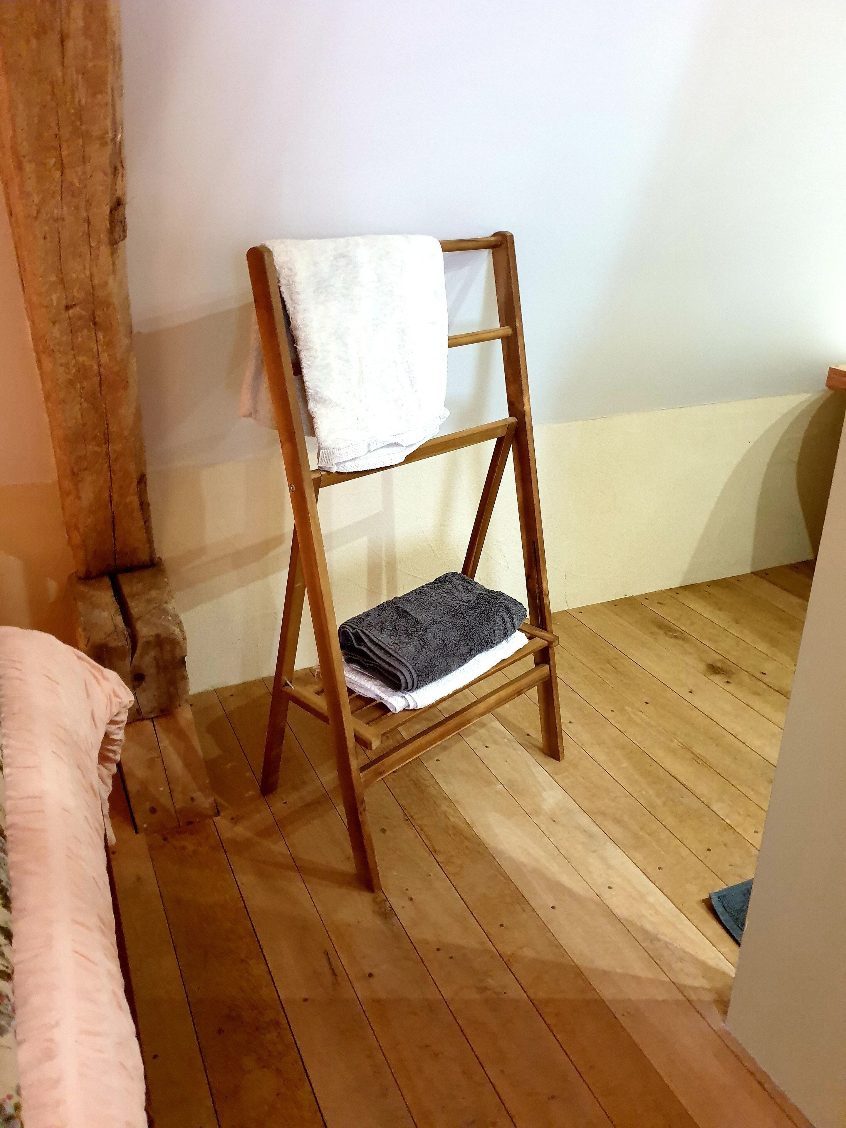 A wooden ladder with towels on it, a wooden floor, and a white wall.