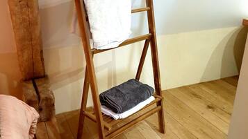 A wooden ladder with towels on it, a wooden floor, and a white wall.
