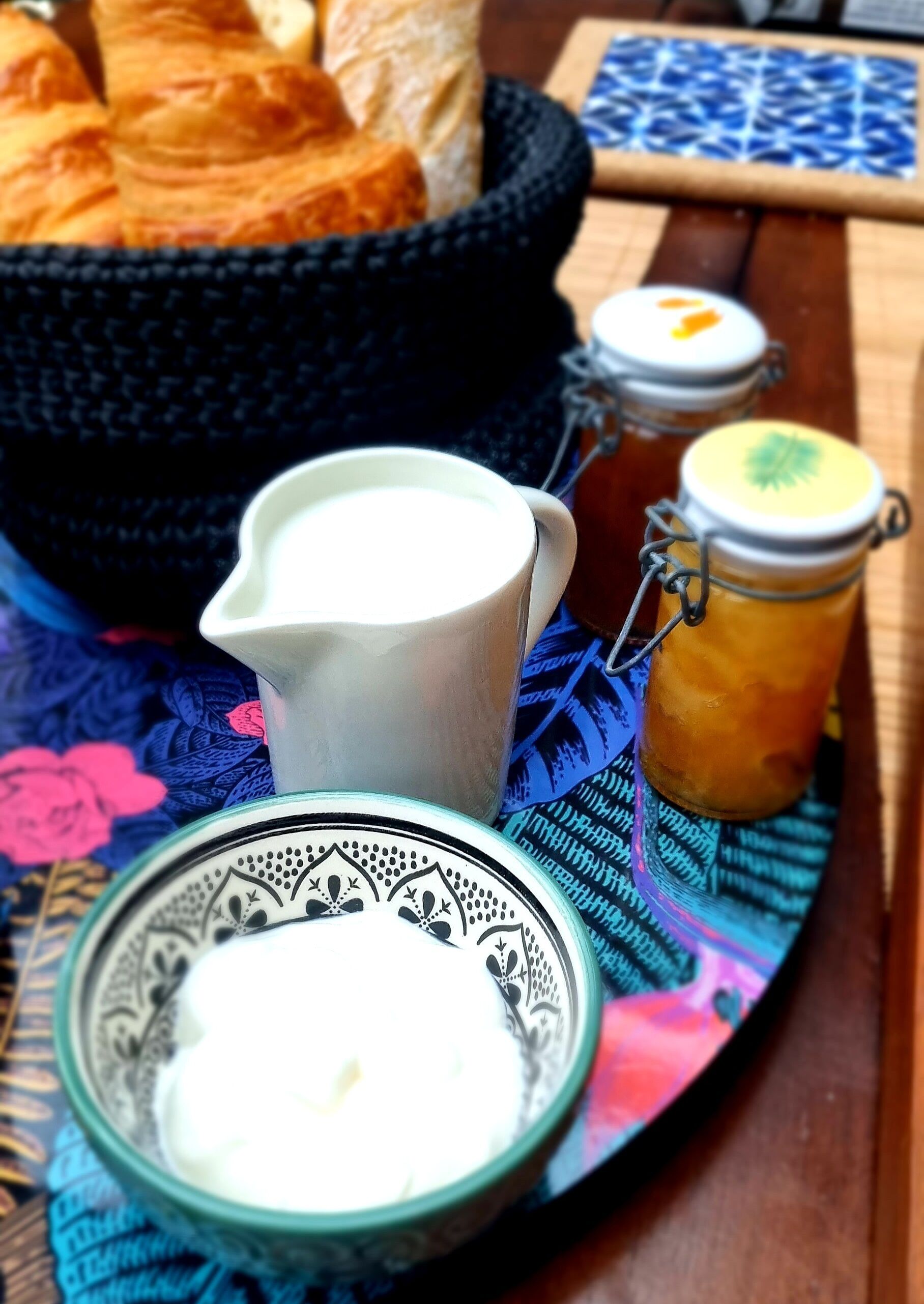 Taula amb un bol de croissants, una gerra de llet, un pot de melmelada i un plat decoratiu.