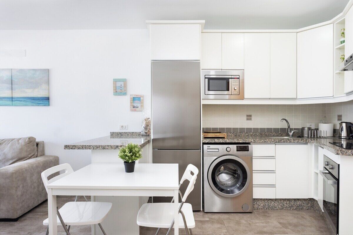 A compact kitchen with a refrigerator, microwave, washing machine, and a dining area with a table and chairs.
