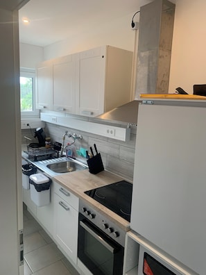 A modern kitchen with white cabinets, a stainless steel sink, a built-in oven, and a black stovetop.