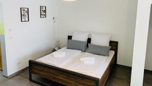 Un dormitorio moderno con una cama de madera, ropa de cama blanca y una lámpara colgante negra.