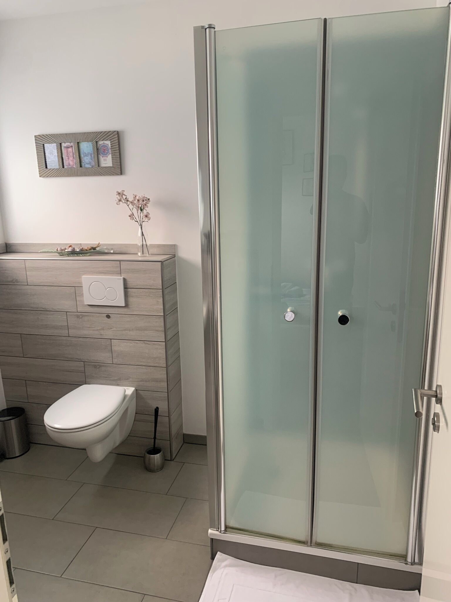 Et stilfuldt badeværelse med en glasbrusekabine, toilet og et vaskeområde med spejl og pynteting.