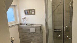 Un baño con inodoro, cabina de ducha de vidrio y un pequeño lavamanos.