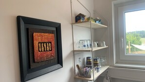 Una habitación con una obra de arte enmarcada en la pared, un estante con diversos objetos y una ventana con vistas.