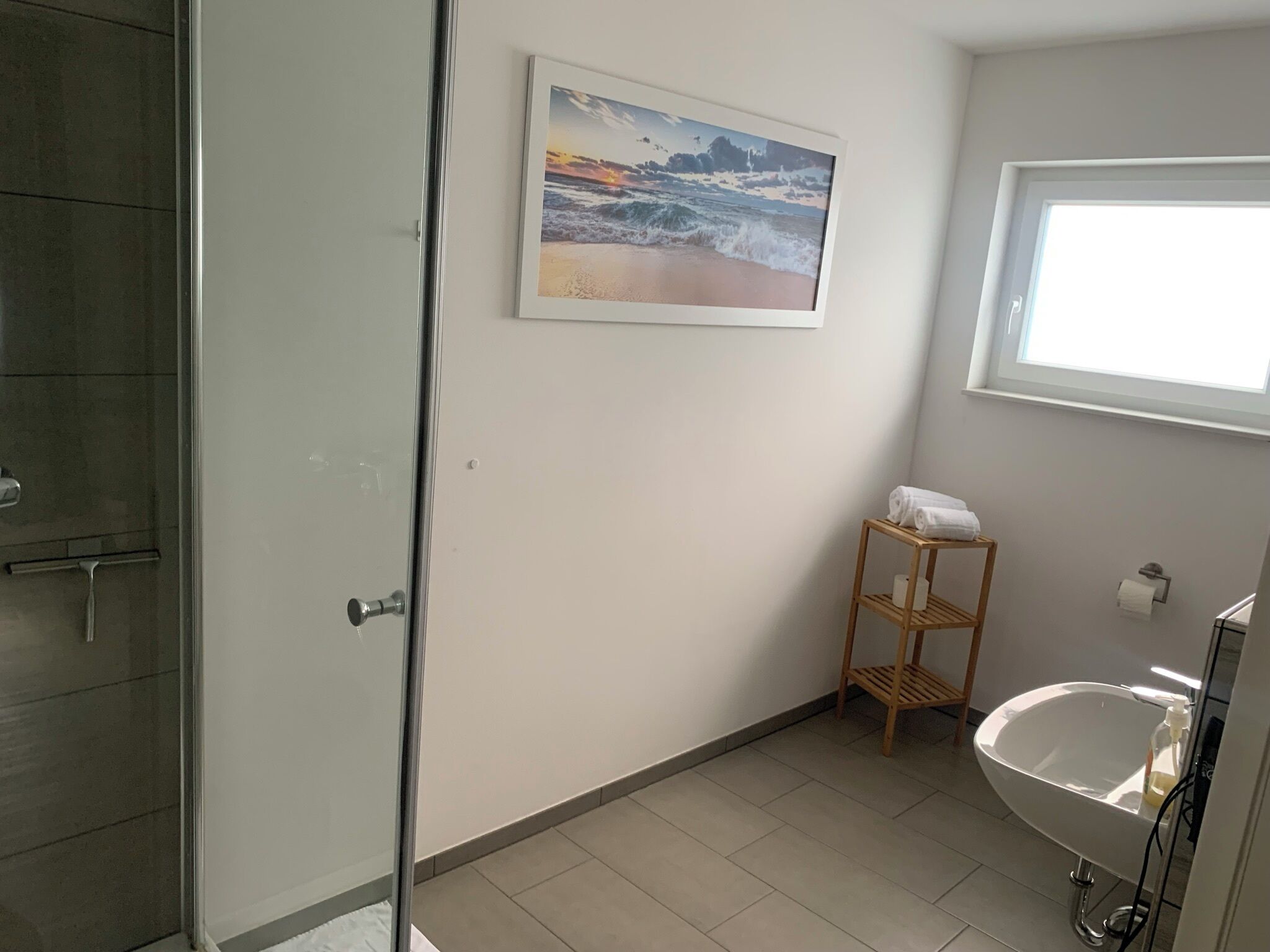 A bathroom with a shower, a sink, a toilet, a towel rack, and a framed picture on the wall.