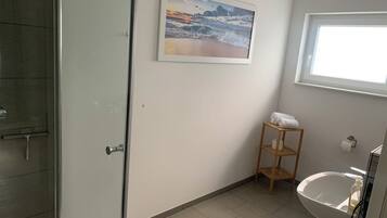 A bathroom with a shower, a sink, a toilet, a towel rack, and a framed picture on the wall.