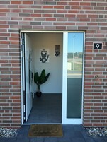 Una entrada de edificio con puerta de cristal, una planta en maceta y dos cuadros en la pared.