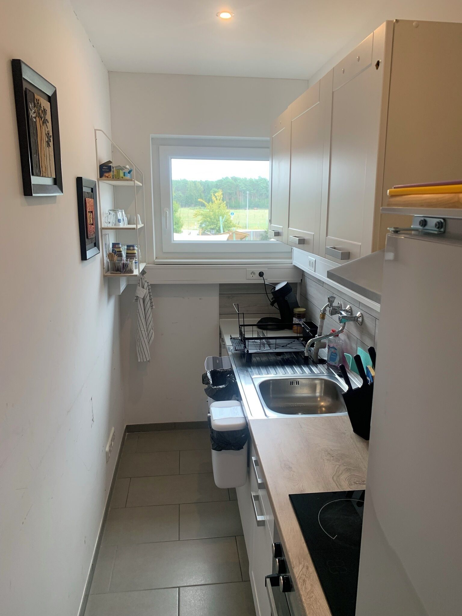 Una cocina compacta con ventana, armarios blancos y horno empotrado.